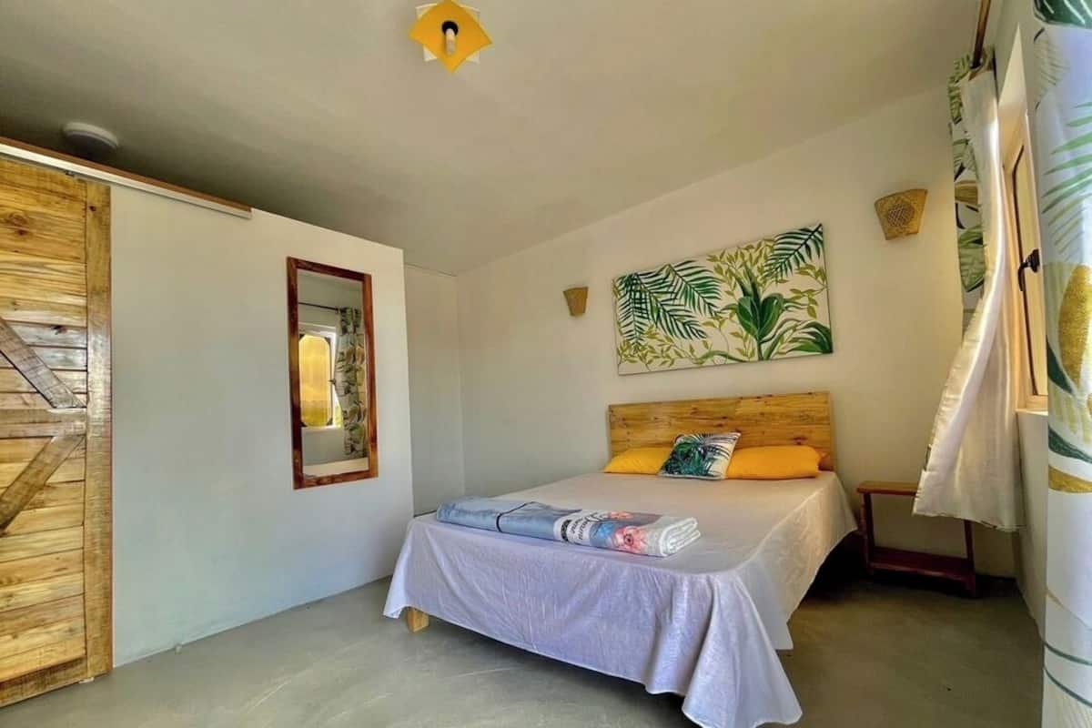 A bedroom with a bed, a wooden door, a mirror, a painting, and a small table.
