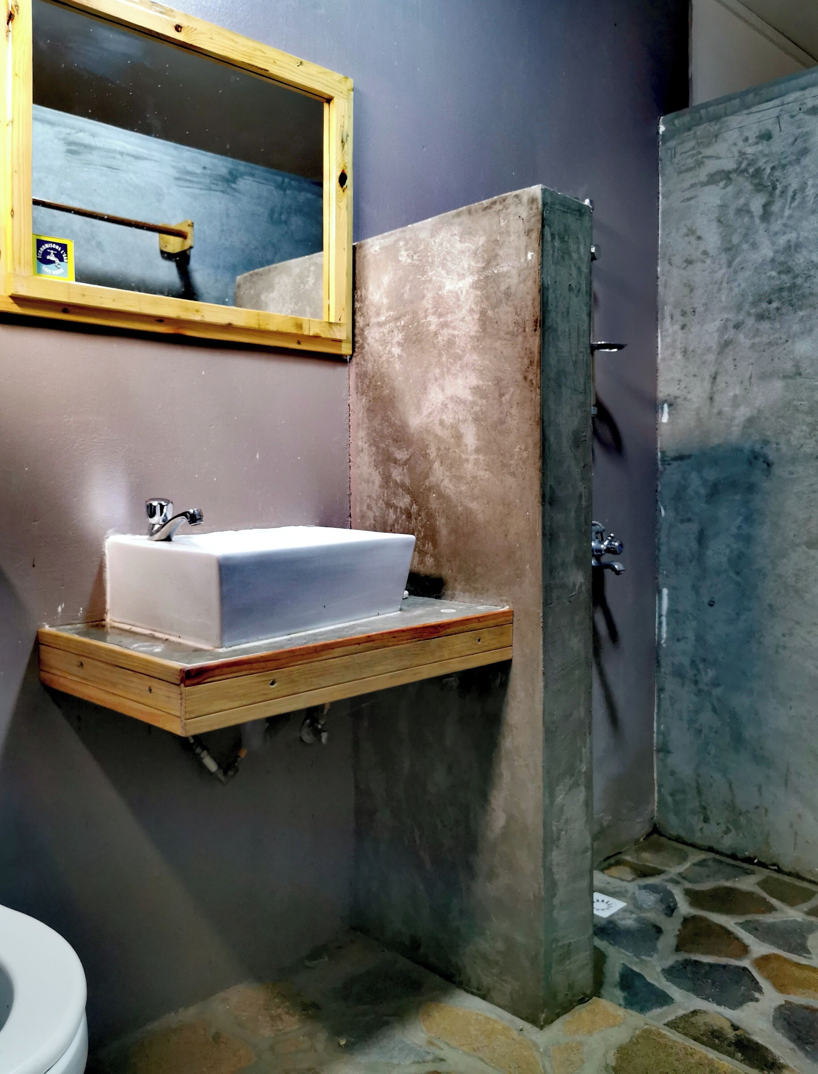 A bathroom with a wooden vanity, a white sink, a mirror, and a shower area.