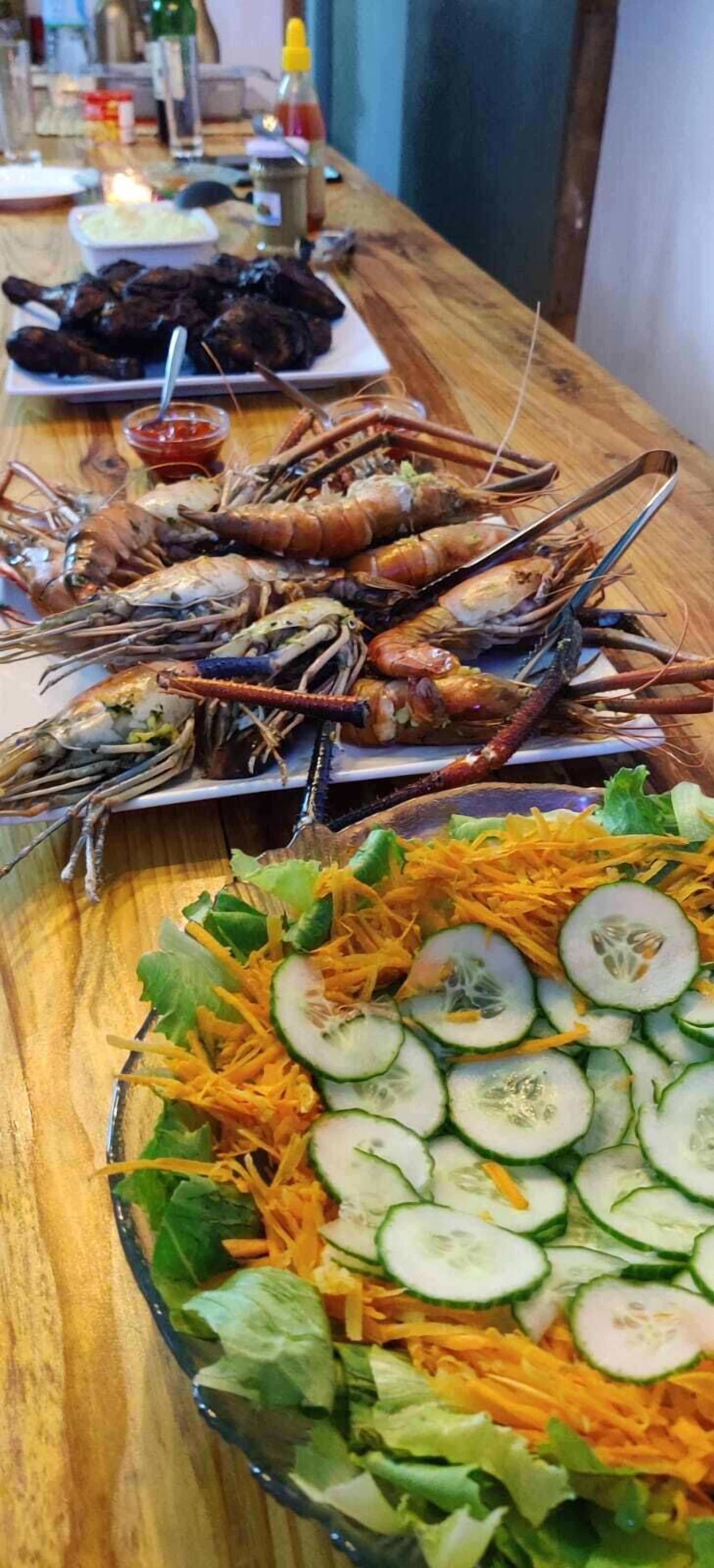 Een tafel met zeevruchten, waaronder garnalen en een salade met komkommers en wortel.