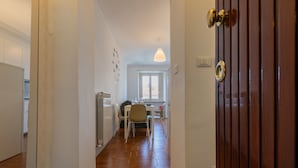 A hallway leading to a dining area with a table and chairs, a window, and a door with a handle. - Il Papiro Apartment by Wonderful Italy (Turin)