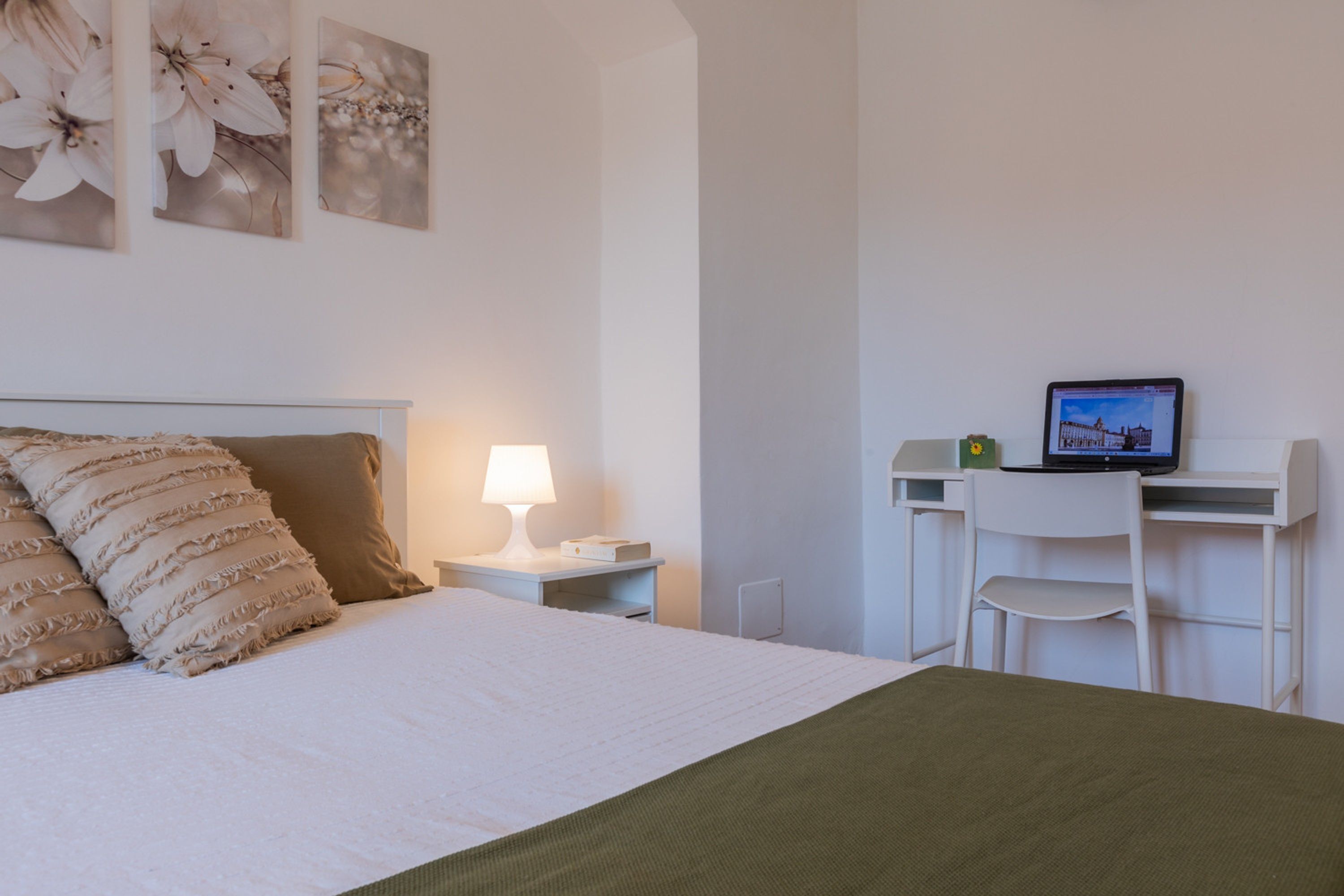 A bedroom with a bed, a desk with a laptop, a chair, and a lamp.