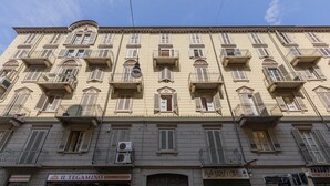 A multi-story building with balconies, a shop on the ground floor, and a closed shutter on the right. - Il Papiro Apartment by Wonderful Italy (Turin)