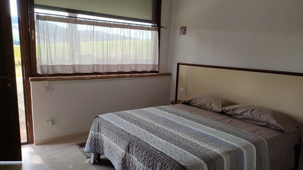 A bedroom with a bed, a window with curtains, and a door. - ElsAnto-beb (San Venanzo)