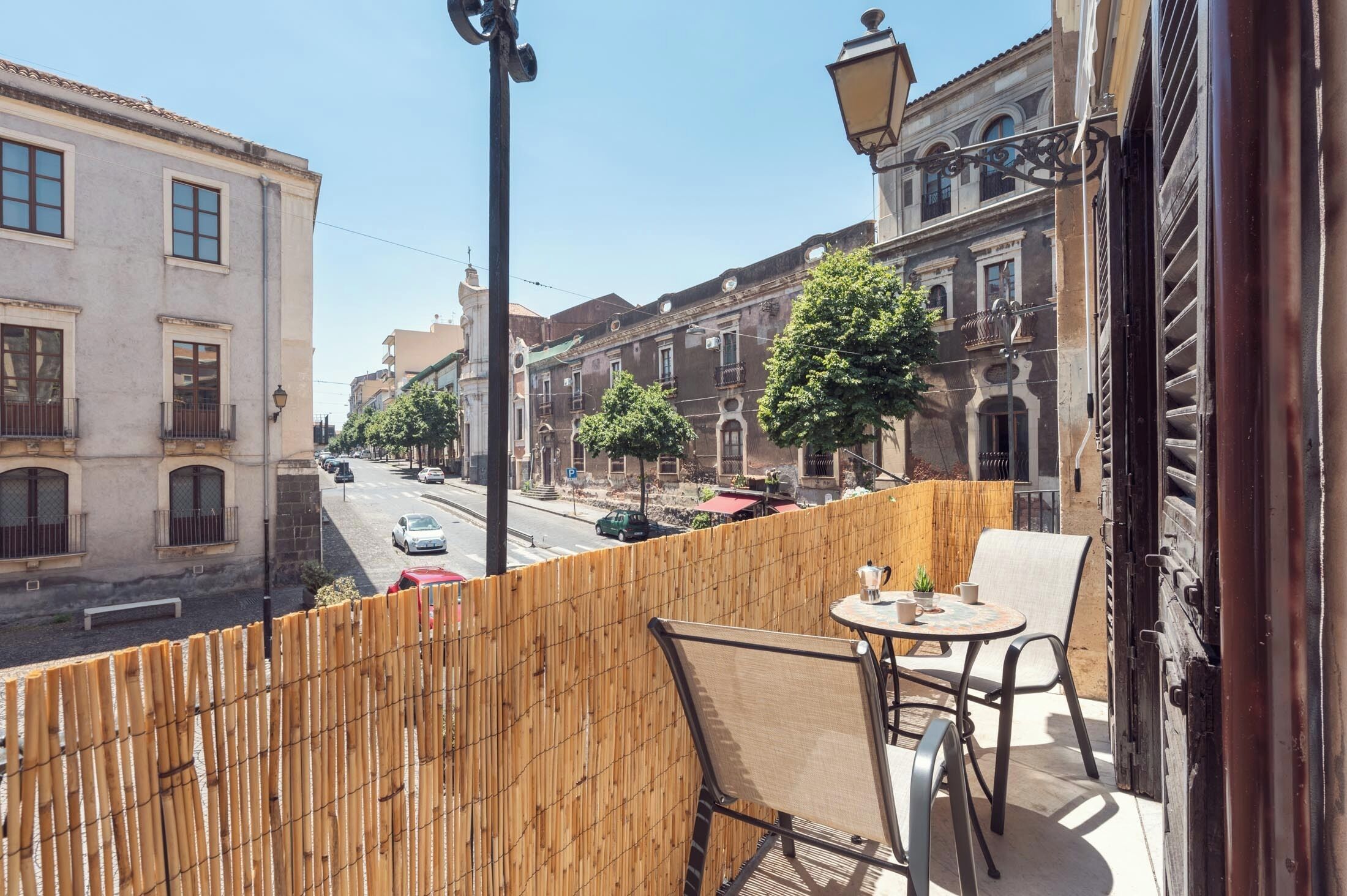 Ein Balkon mit Blick auf eine Straße, gesäumt von historischen Gebäuden, einem Tisch mit Stühlen und einem kleinen Blumentopf.