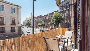 Ein Balkon mit Blick auf eine Straße, gesäumt von historischen Gebäuden, einem Tisch mit Stühlen und einem kleinen Blumentopf.