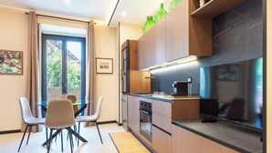 Une cuisine moderne avec des meubles en bois, un plan de travail noir et un four encastré. On y trouve un coin repas avec une table et des chaises en verre, ainsi qu’une fenêtre avec des rideaux.