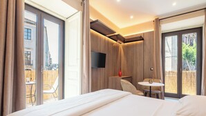 Une chambre d’hôtel avec un grand lit, une petite table avec une chaise, un téléviseur fixé au mur et une porte-fenêtre coulissante donnant sur un espace extérieur.