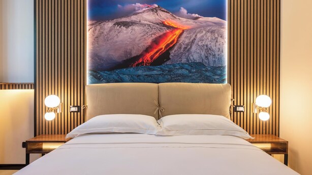 Une chambre d’hôtel avec un grand tableau représentant un volcan accroché au mur, un lit avec du linge de lit blanc et deux lampes de chevet.
