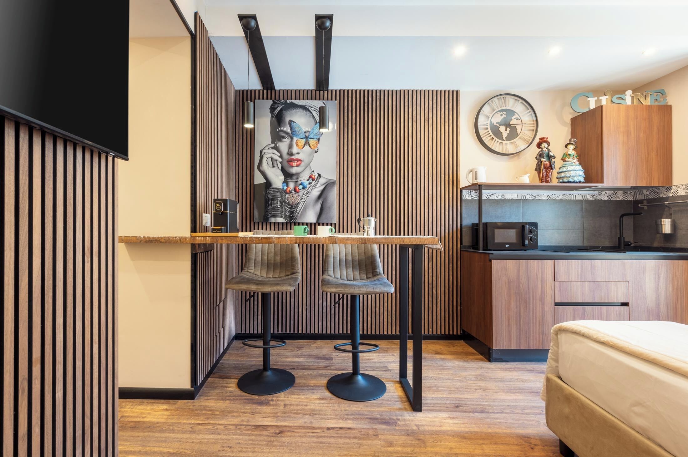 Una cocina moderna con encimera de madera, dos taburetes de bar, una mesa de comedor y un reloj en la pared.