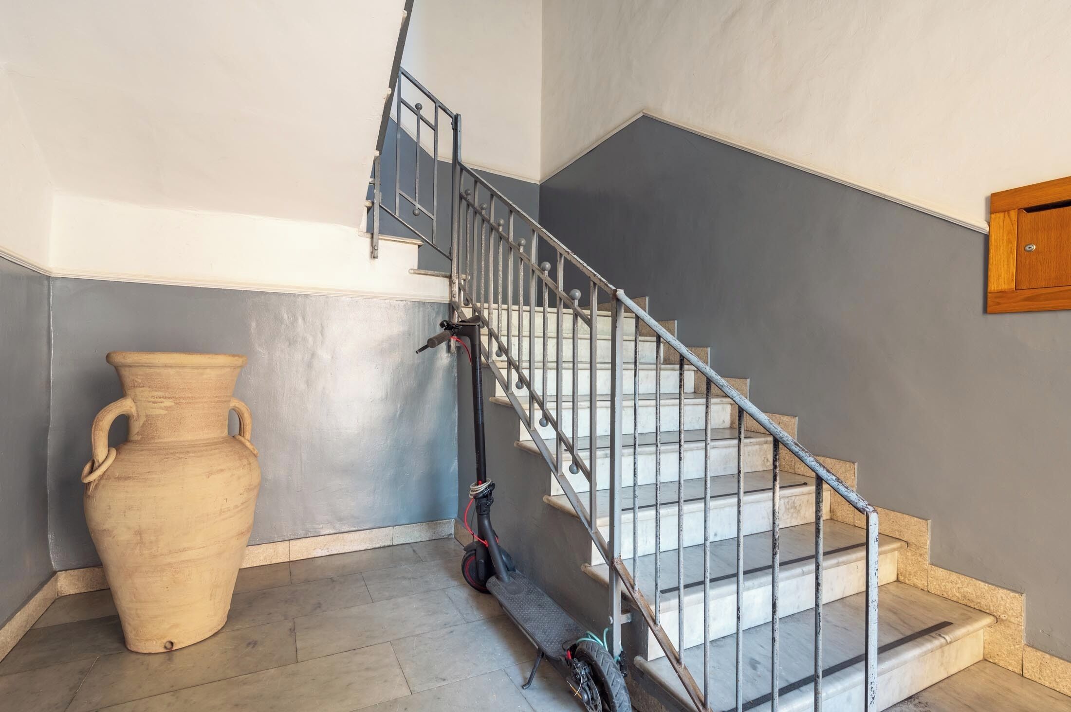 Una escalera con barandilla de metal, un jarrón grande y una patineta.