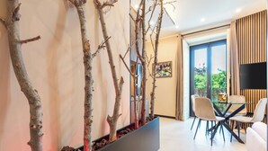 Un salon moderne comprenant un coin repas, un grand pot noir orné de branches et une grande fenêtre offrant une vue dégagée.