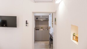 A narrow hallway with a flat-screen TV on the left, a kitchen area with cabinets and a sink, and a small table with a plant on the right. - Barlaman Luxury Rooms (Palermo)