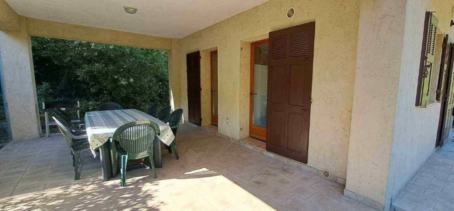 An outdoor patio with a table and chairs, a door, and a wall with a window.