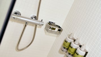 A shower area with a handheld showerhead, a wall-mounted control, and a soap dispenser.