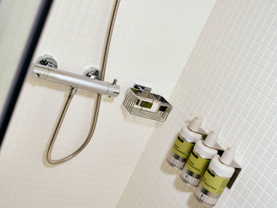 Een douchecel met douchekop, bediening aan de muur en een zeepdispenser.