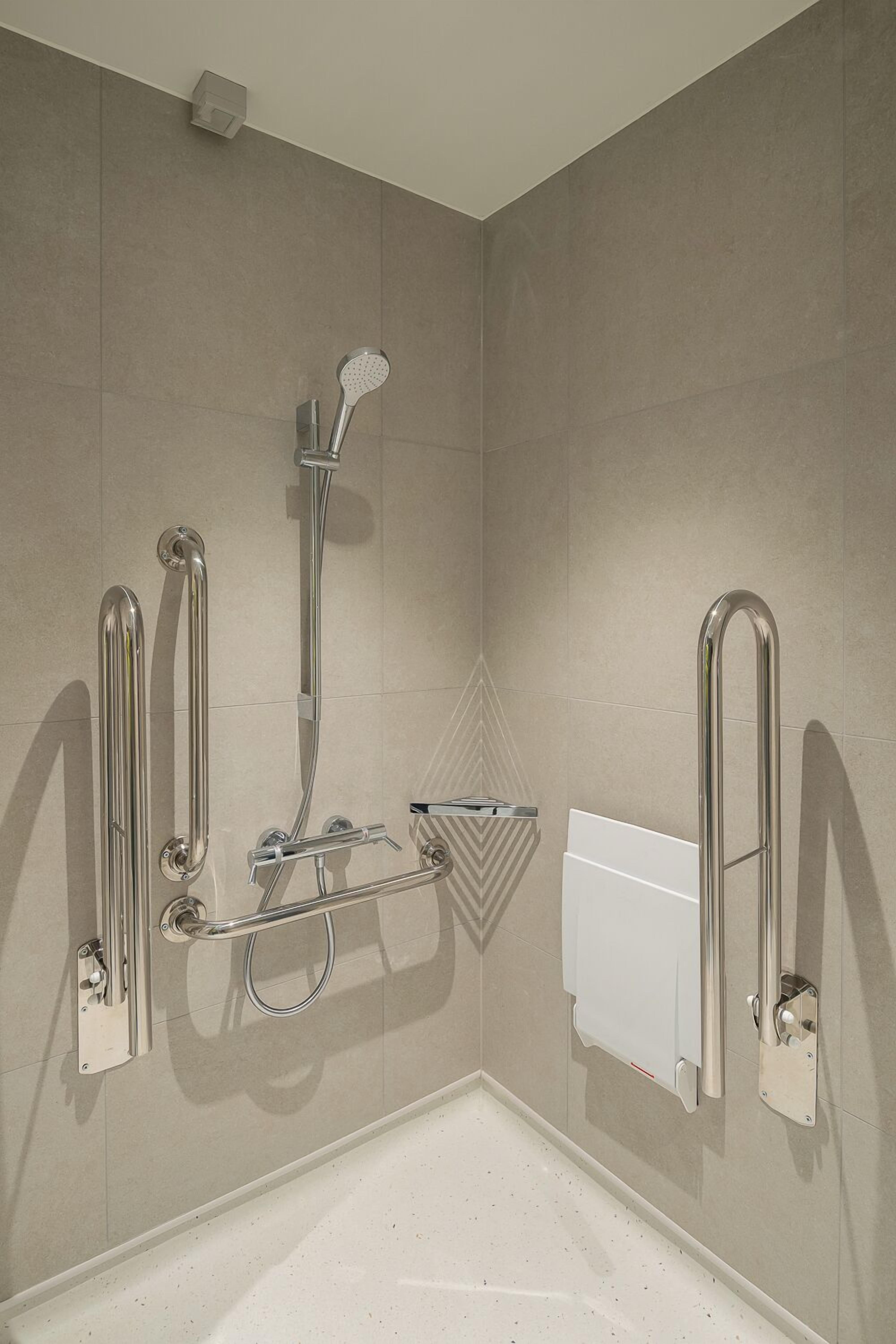 Une salle de bain moderne dotée d’une douche à l’italienne, de barres d’appui et d’un pommeau de douche amovible.