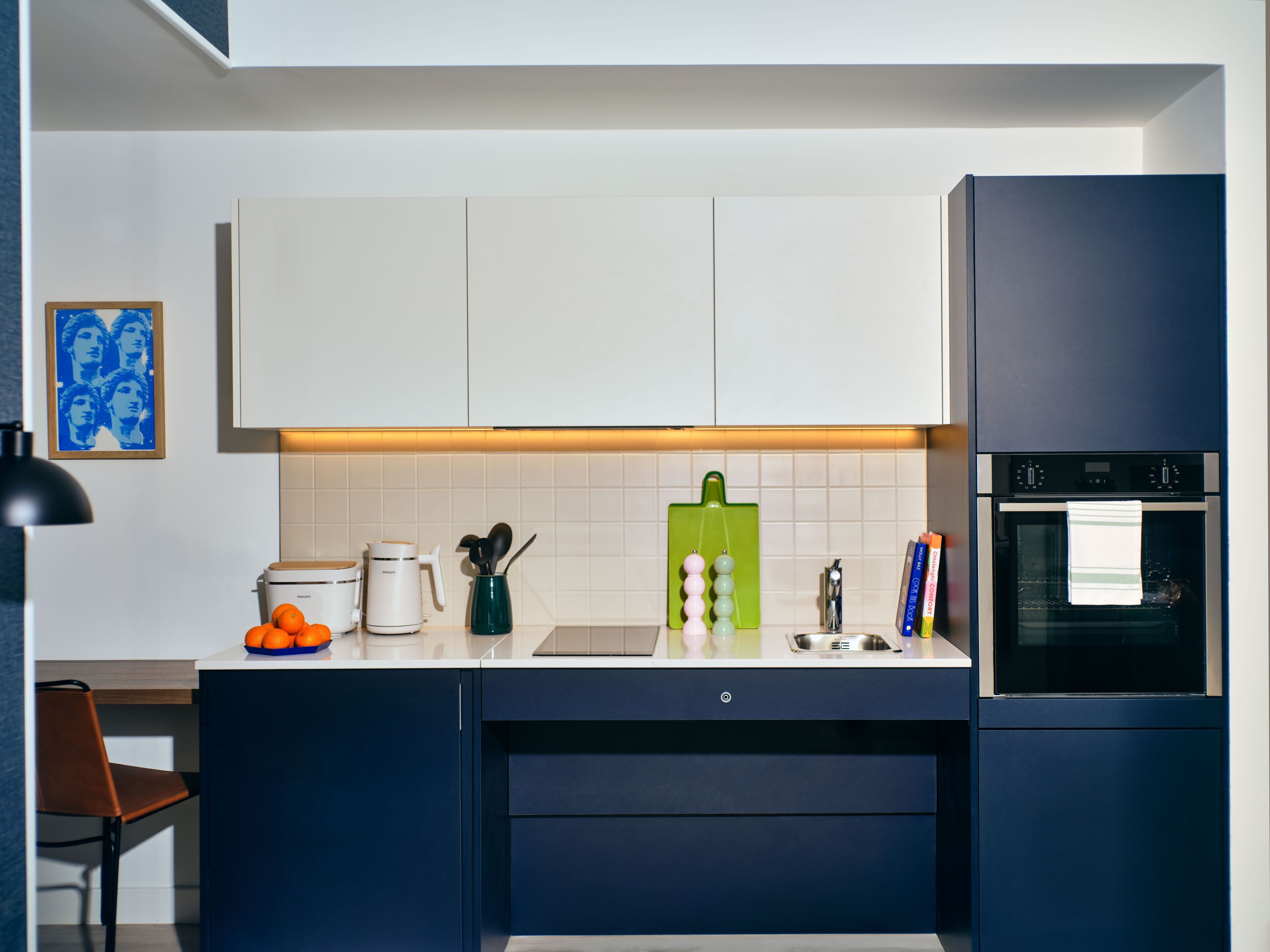 A modern kitchen with white cabinets, a green cutting board, and a built-in oven.