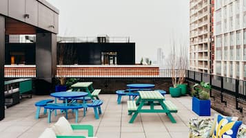 Une terrasse sur le toit, aménagée avec des espaces de détente en plein air, comprenant des tables et des chaises, et offrant une vue sur le paysage urbain.