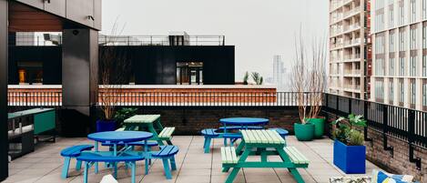 Terraza en la azotea con mobiliario exterior, incluyendo mesas y sillas, y vistas de un paisaje urbano.