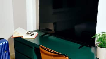 Una habitación moderna con un escritorio verde, un televisor negro, una maleta azul y un cuadro en la pared.