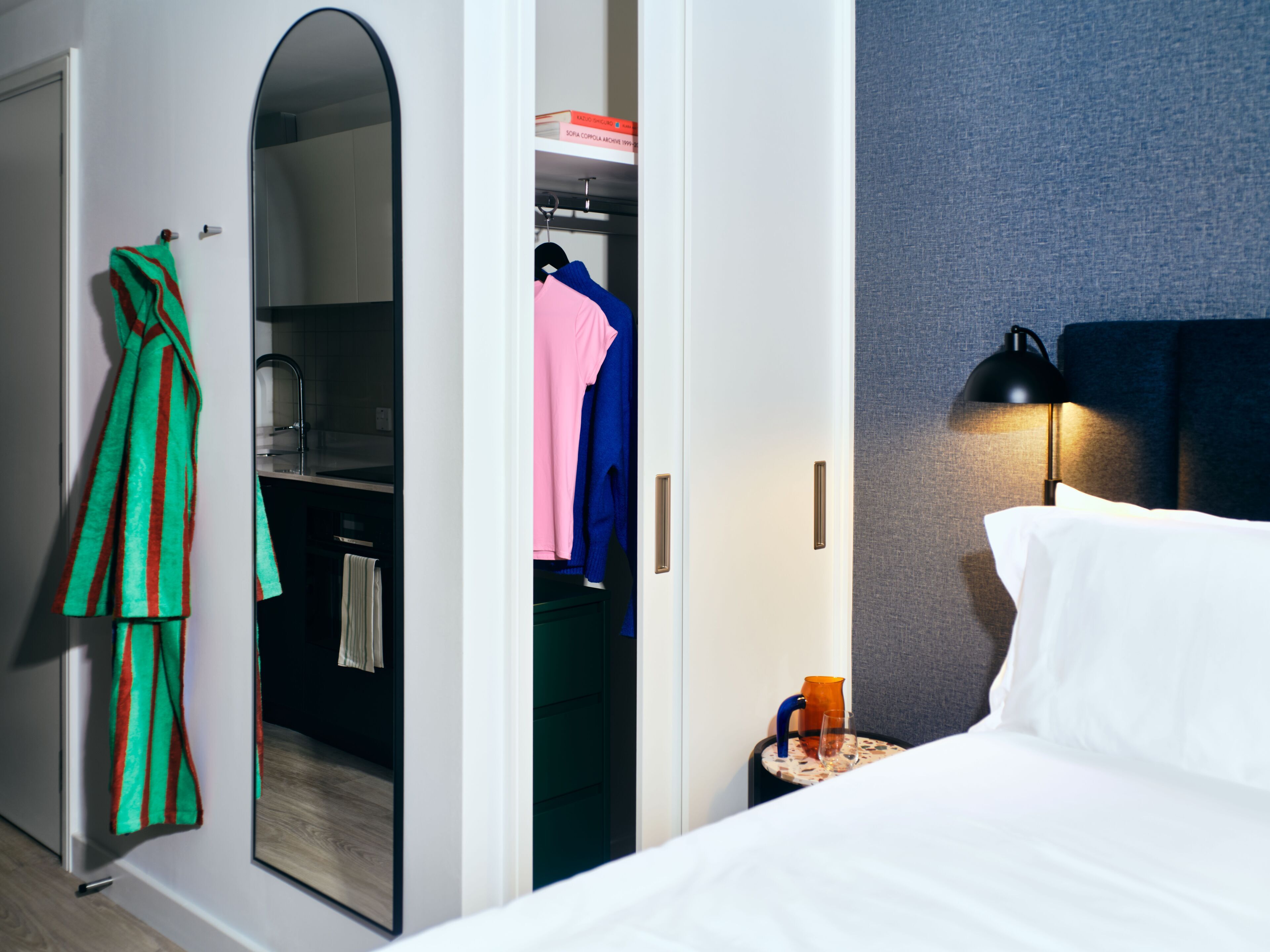 A hotel room with a bed, a bedside table with a lamp, a wardrobe, and a mirror.