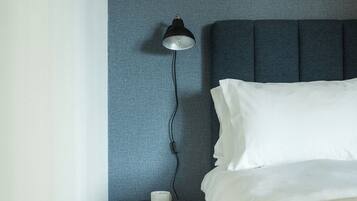A neatly made bed with white sheets and a pillow, a bedside table with a lamp, and a wall with a textured pattern.