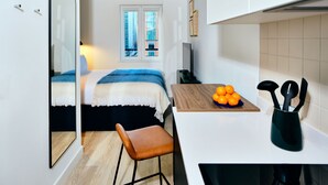 A compact hotel room with a bed, a small seating area, a kitchenette, and a window with a city view. - Vertus Edit Canary Wharf (London)