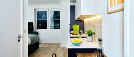 A modern kitchen with a wooden floor, a dining table with a bowl of lemons, a book, and a wine bottle.