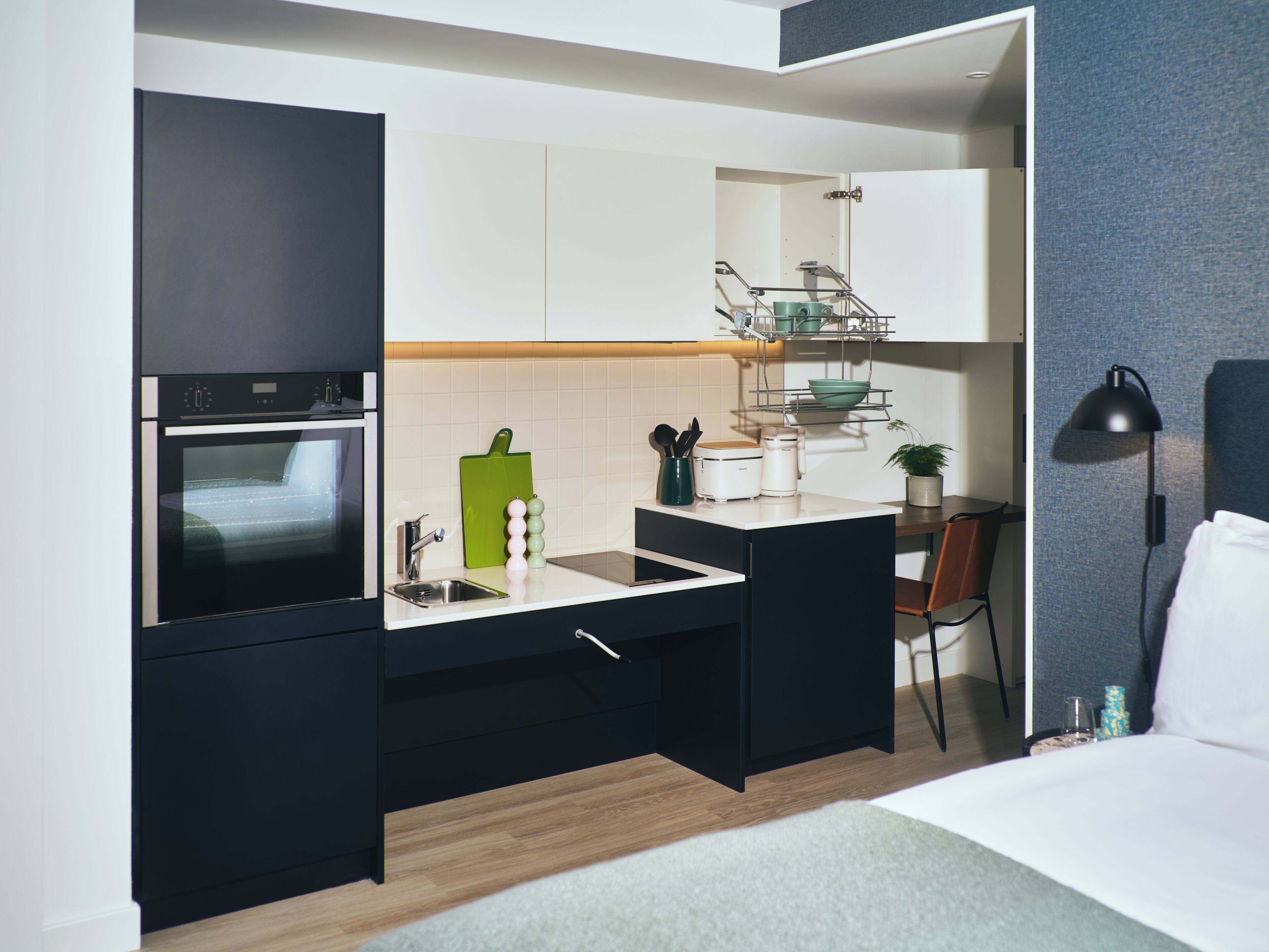 A compact kitchen with a built-in oven, a sink, and a small dining area with a chair.
