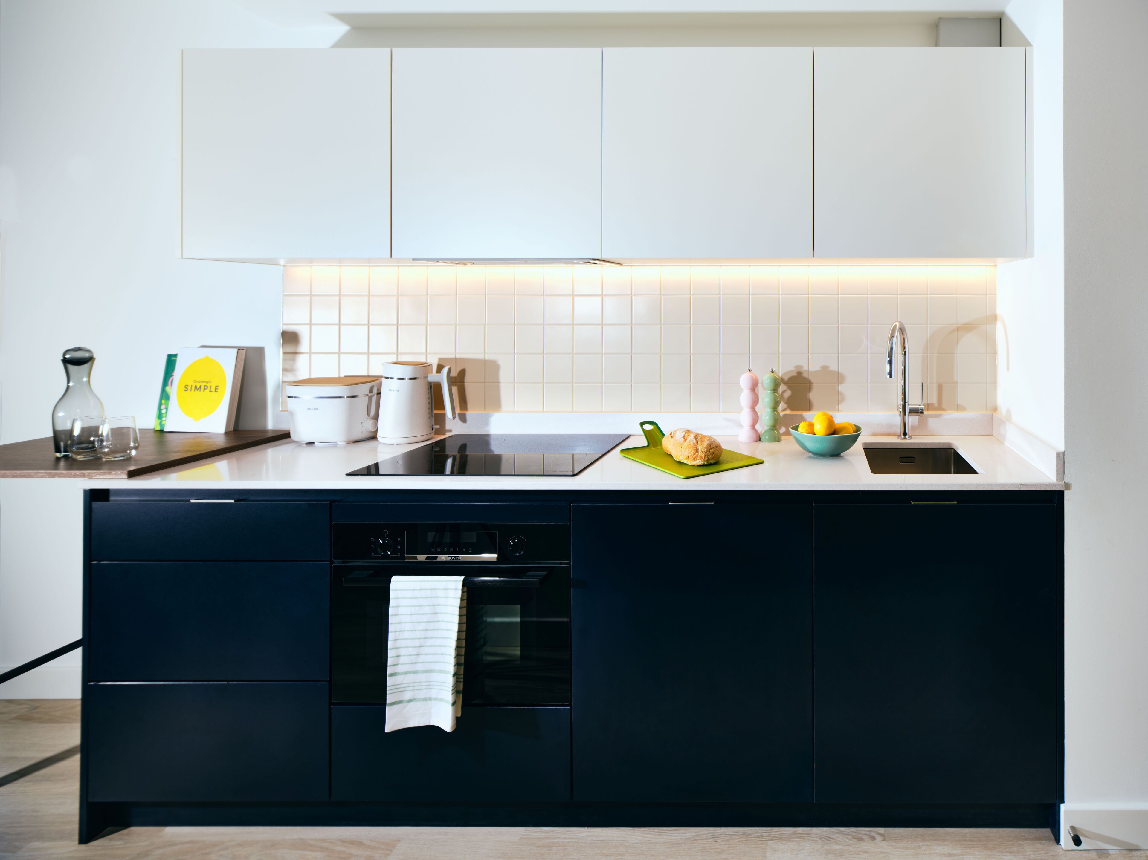 A modern kitchen with a built-in oven, a sink, and a countertop with various appliances and a bowl of lemons.