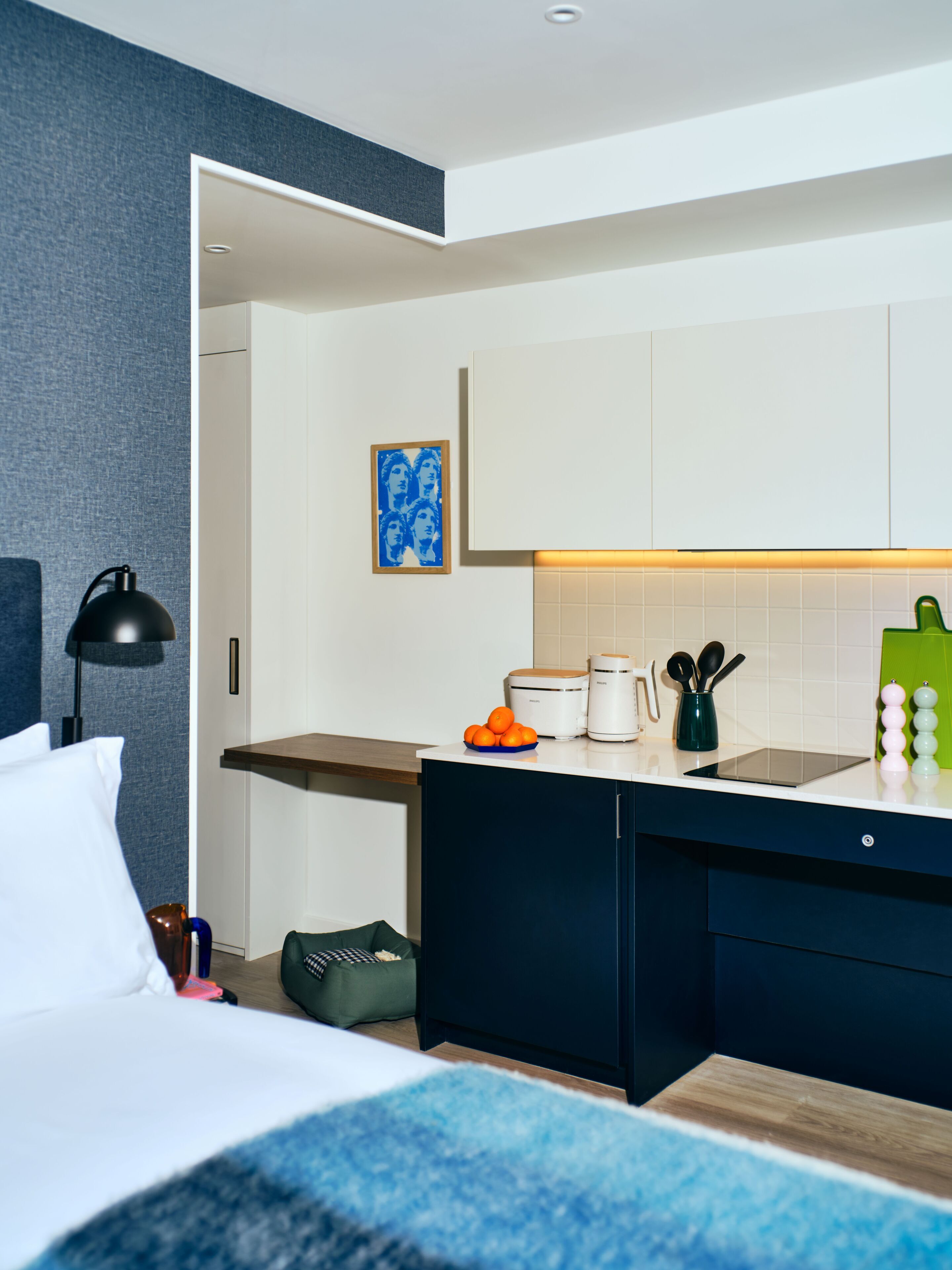 Une chambre d’hôtel moderne équipée d’un lit, d’un bureau, d’un petit coin cuisine et d’une salle de bain.