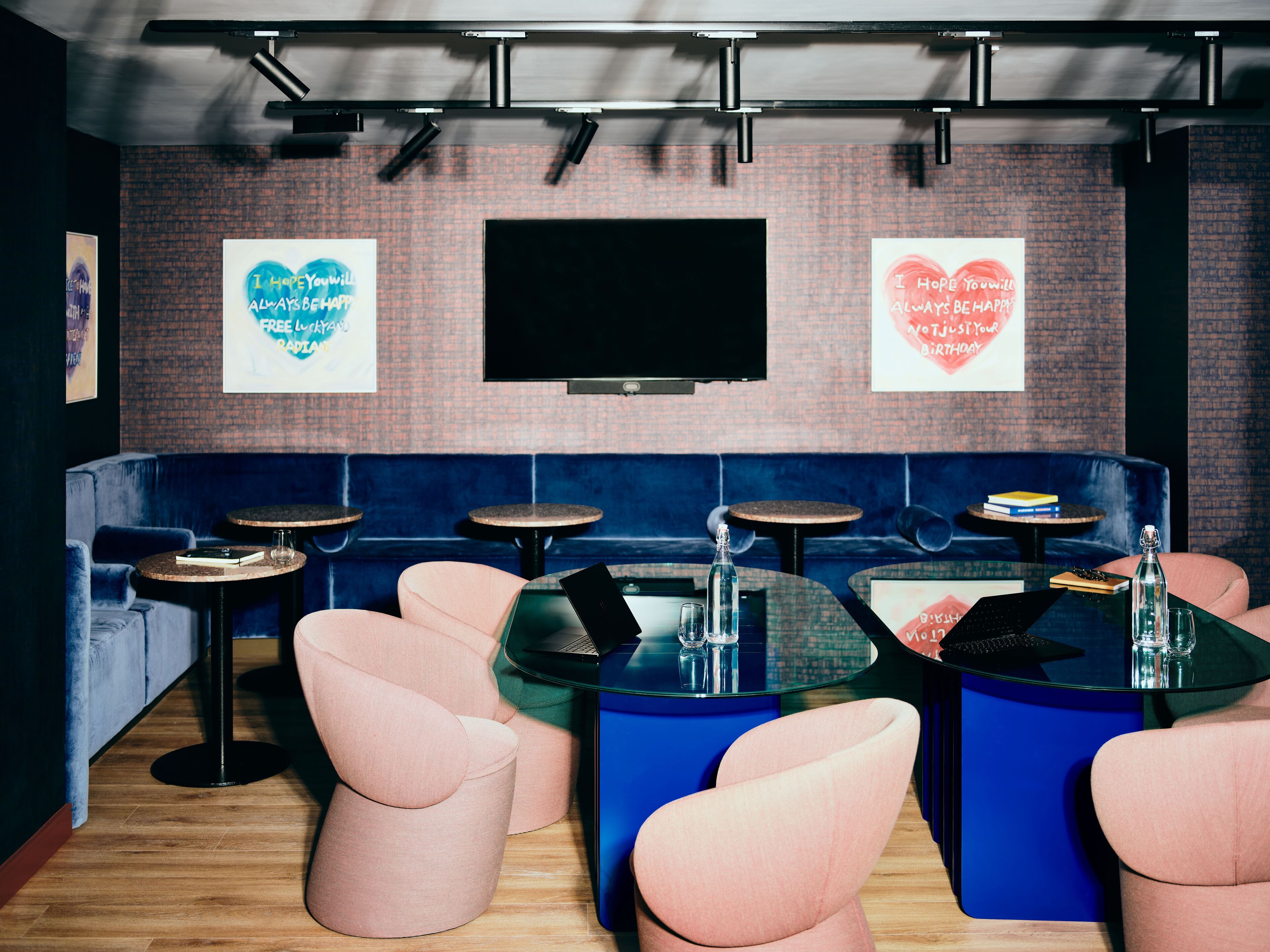 Un salón moderno con asientos azules y rosados, un televisor de pantalla plana y carteles motivacionales en la pared.