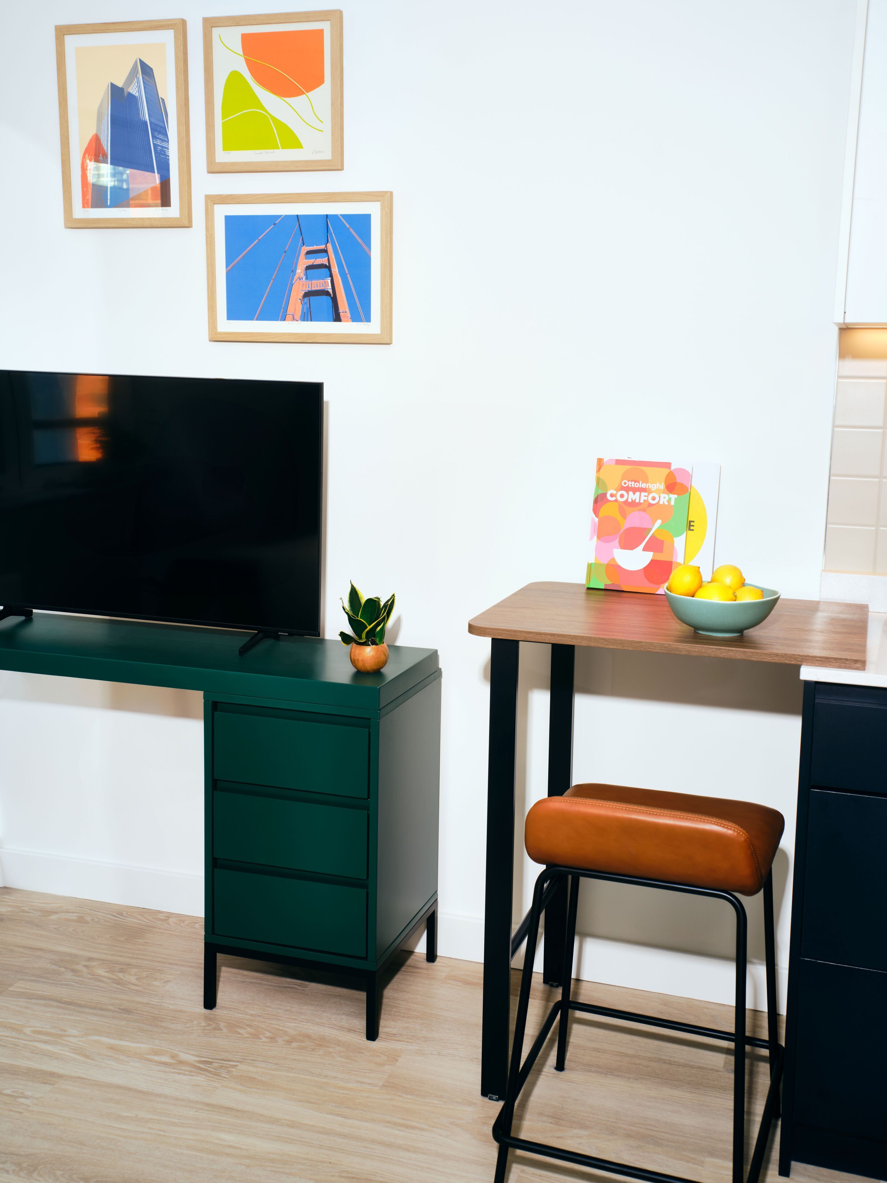 A modern living room with a TV, a green cabinet, a wooden table with a bowl of fruit, and a bench.