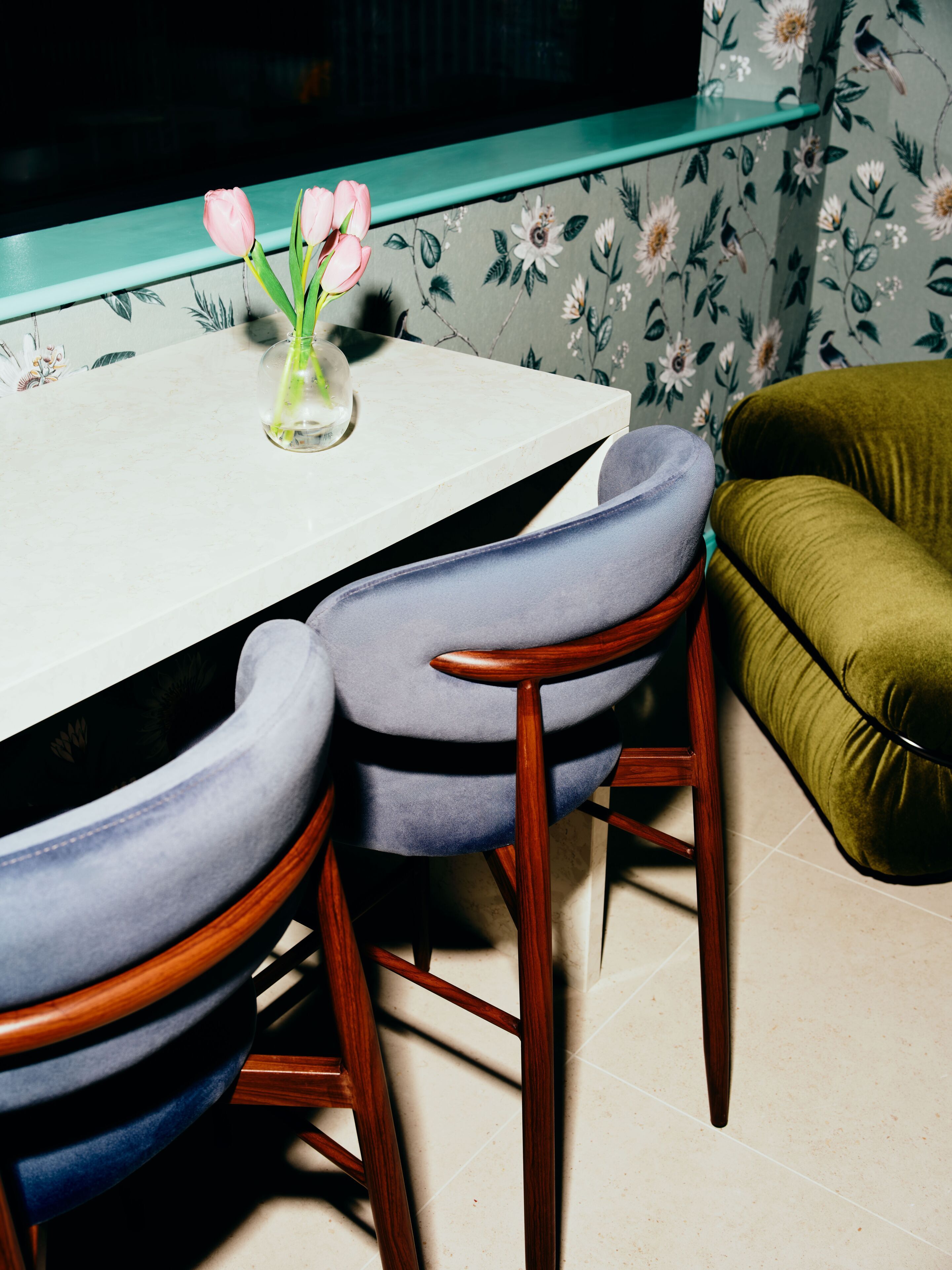 A dining table with a vase of pink flowers, two upholstered chairs, and a green sofa.