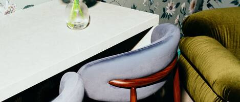 A dining table with a vase of pink flowers, two upholstered chairs, and a green sofa.