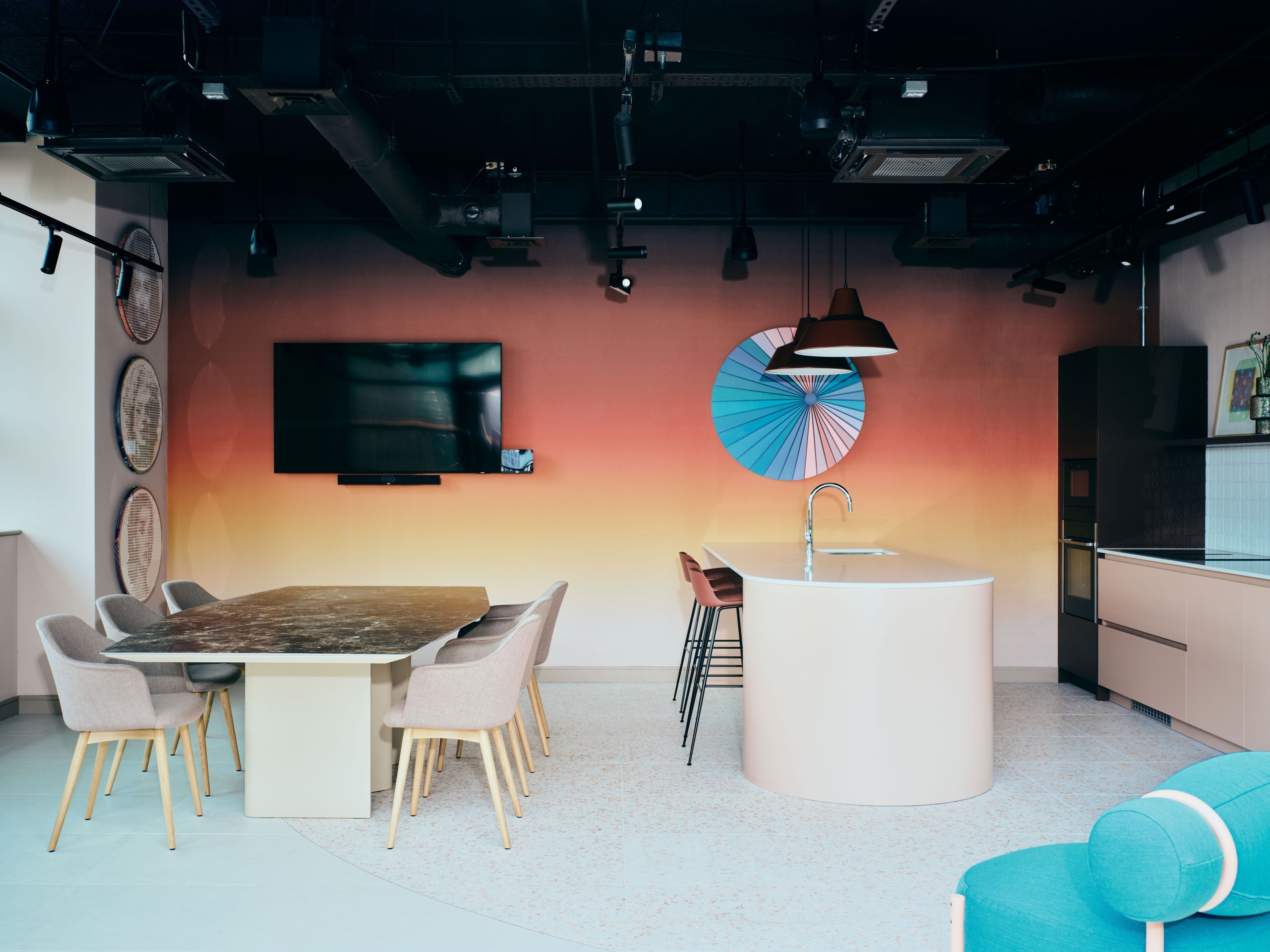 Een moderne keuken met een centraal eiland, een eethoek met tafel en stoelen, een aan de muur bevestigde televisie en een bijzondere plafondventilator.