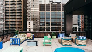 A rooftop terrace with outdoor seating, a glass table, and a view of high-rise buildings. - Vertus Edit Canary Wharf (London)