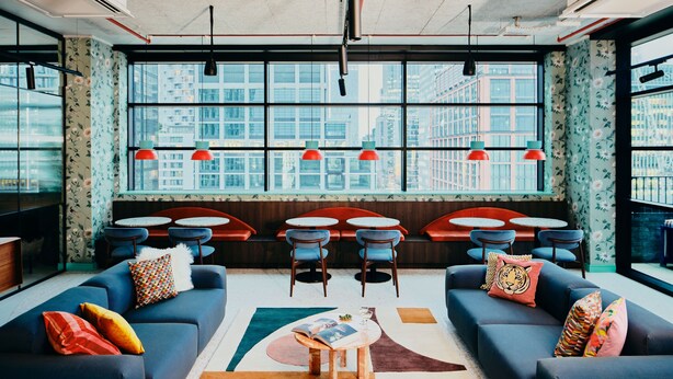 A modern lounge with sofas, tables, and a large window offering a city view. - Vertus Edit Canary Wharf (London)