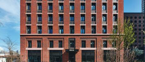 A multi-story brick building with a modern facade, large windows, and a visible entrance with a sign.