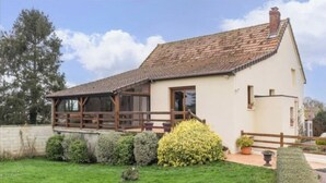 A single-story house with a sloped roof, a wooden deck, and a well-maintained garden. - Capucine's house (Les Moutiers-en-Cinglais)