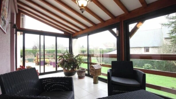 A covered patio with wicker furniture, large windows, and a view of the outdoors. - Capucine's house (Les Moutiers-en-Cinglais)