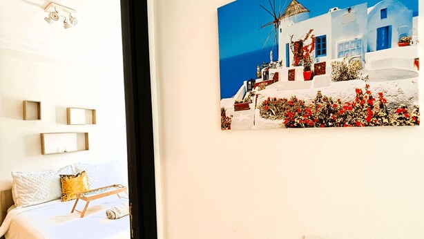 A bedroom with a bed, bedside tables, and a painting of a white building with red flowers. - Confort Moderne in the heart of Salé, near train station and airport (Rabat- Sale')