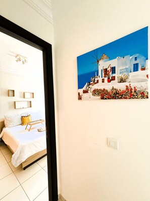 A bedroom with a bed, bedside tables, and a painting of a white building with red flowers. - Confort Moderne in the heart of Salé, near train station and airport (Rabat- Sale')