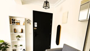 A living room with a black door, a white bookshelf, a grey sofa with blue cushions, and a skateboard leaning against the wall. - Confort Moderne in the heart of Salé, near train station and airport (Rabat- Sale')