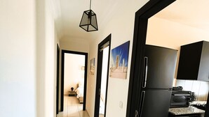 A narrow hallway leading to a bedroom with a door, a kitchen area with a washing machine, and a dining area with a table and chairs. - Confort Moderne in the heart of Salé, near train station and airport (Rabat- Sale')