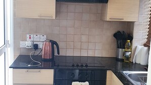 Eine Küche mit Herd, Backofen und Wasserkocher. Es gibt Schränke, eine Arbeitsplatte und ein Fenster.