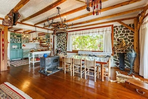 A rustic kitchen with wooden beams, a stone wall, and a large window with a view of greenery.