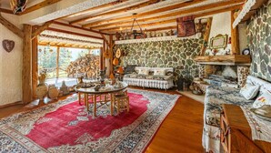 Ein rustikales Interieur mit Steinwand, Holzbalken, Kamin und einem Essbereich mit rotem Teppich.