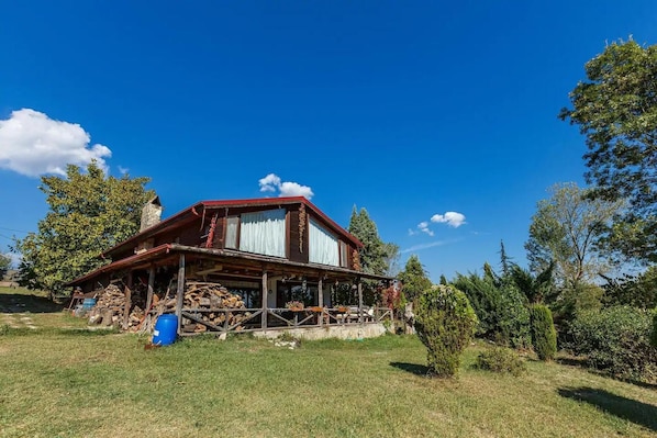 A rustic wooden house with a porch, surrounded by trees and a clear blue sky.