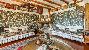 Ein gemütlicher Raum mit Steinwänden, Holzbalken und einem zentralen Kamin. Zwei Sofas mit floralem Bezug und ein Couchtisch mit dekorativen Gegenständen.